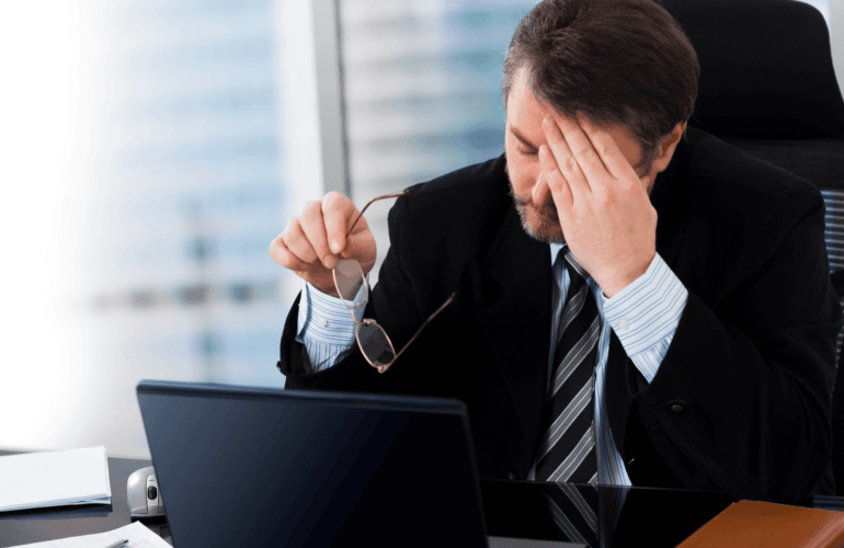 Businessman looking stressed looking at his screen and holding his glasses