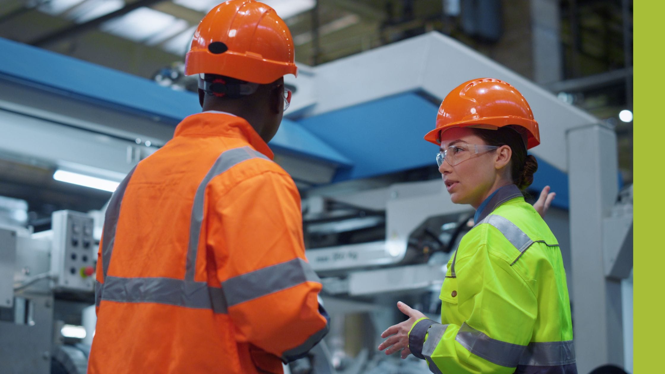 a man and a woman wearing hard harts and high vis, stood in front of automation equipment having a conversation